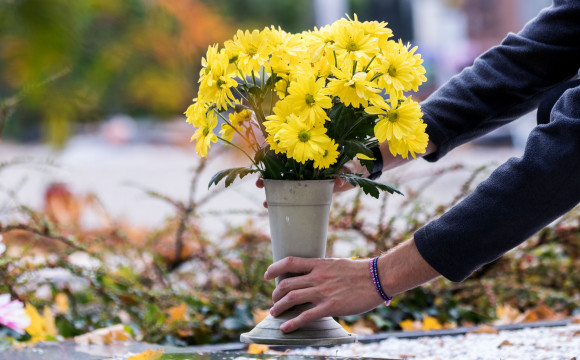 Vaza s šopkom rumenega cvetja, ki jo oseba polaga na grob.
