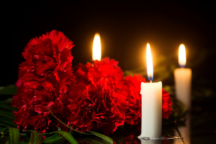 Tri sveče, ki gorijo poleg šopka rdečih rož.